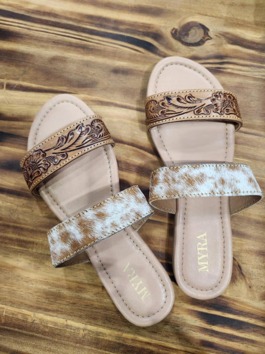 Sandals with tooled leather on one strap and brown and cream colored cowhide on the other strap