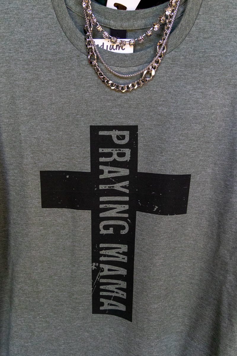 Green t-shirt with a black cross and 'Praying Mama' text, worn with layered necklaces.